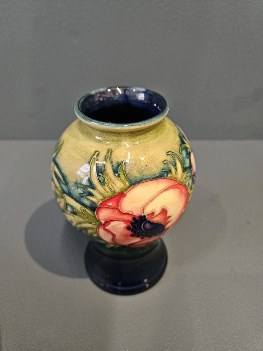 A small baluster-shaped ceramic vase featuring a tubelined red anemone motif against a ground fading from yellow-green to dark blue. View II