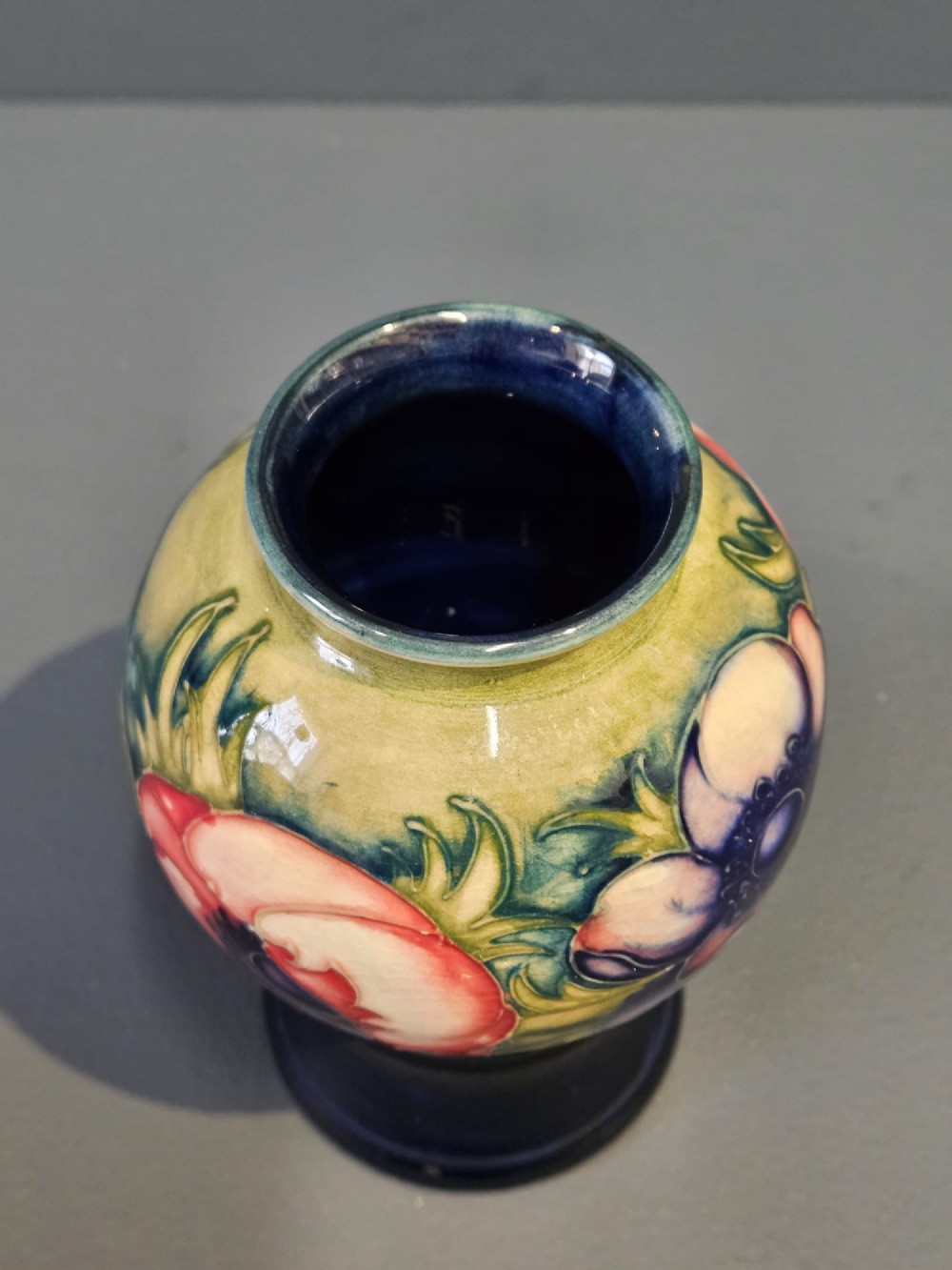 A small baluster-shaped ceramic vase featuring a tubelined red anemone motif against a ground fading from yellow-green to dark blue. View III