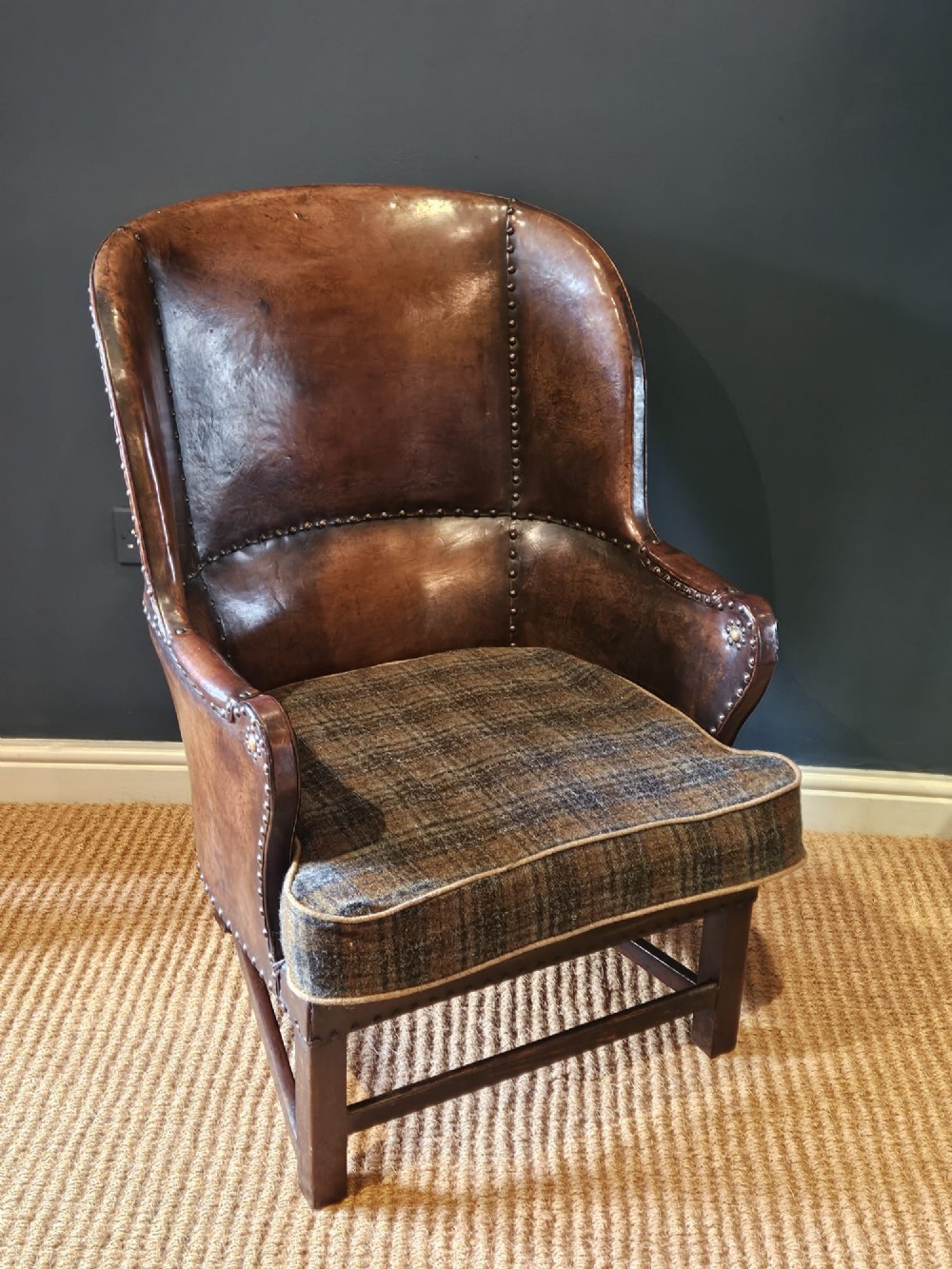 An Arts and Crafts brown leather fireside armchair featuring brass studding, an oak frame, and a woven plaid fabric seat cushion. View II