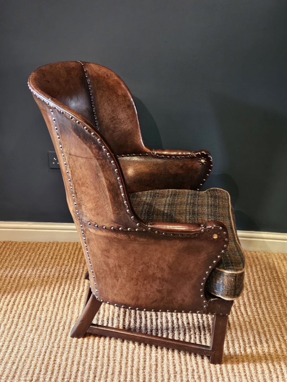 An Arts and Crafts brown leather fireside armchair featuring brass studding, an oak frame, and a woven plaid fabric seat cushion. View III