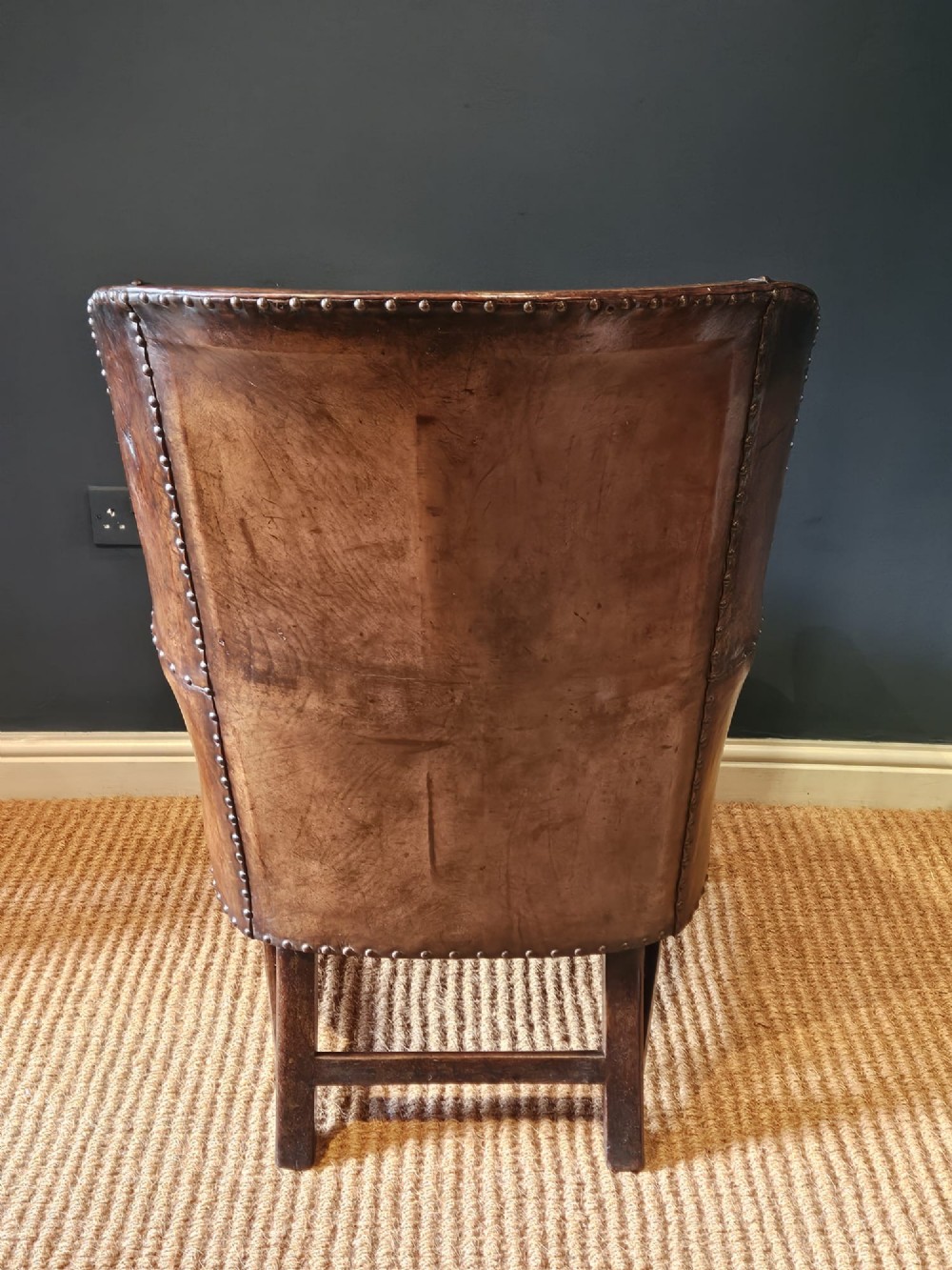 An Arts and Crafts brown leather fireside armchair featuring brass studding, an oak frame, and a woven plaid fabric seat cushion. View V