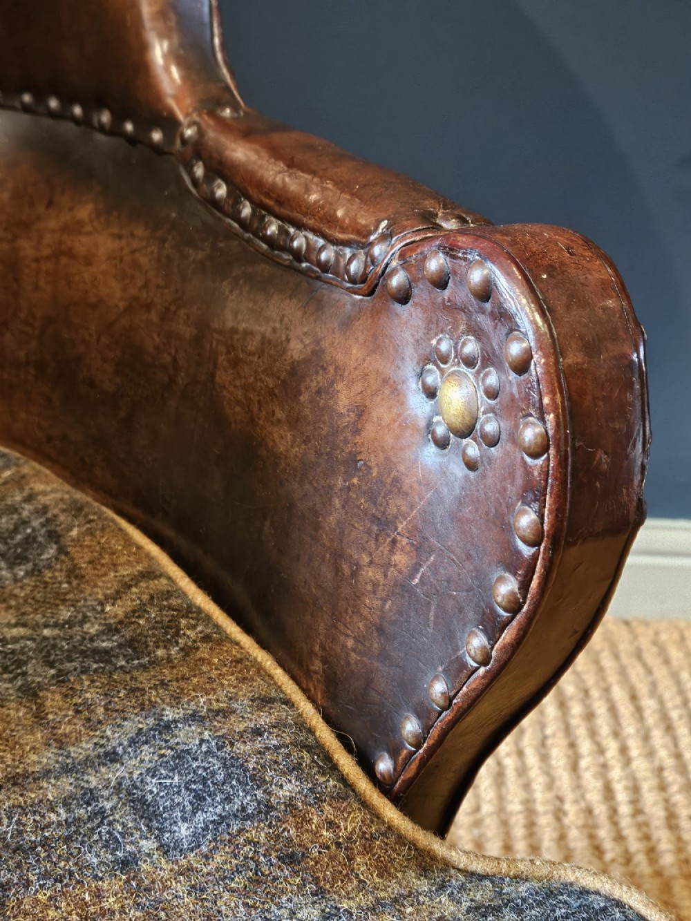 An Arts and Crafts brown leather fireside armchair featuring brass studding, an oak frame, and a woven plaid fabric seat cushion. View X