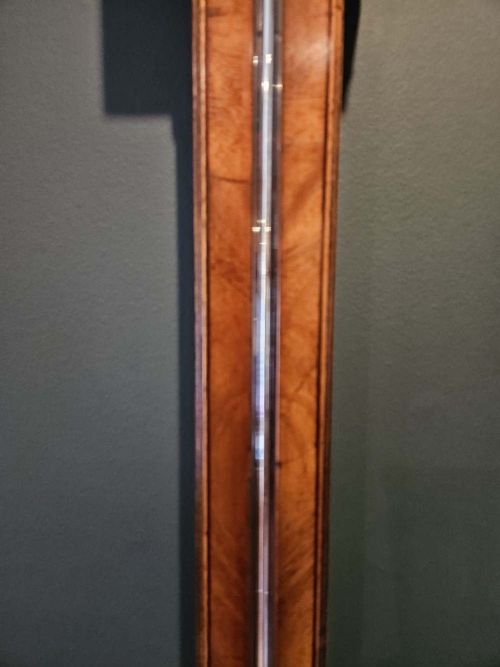 A wall-mounted Georgian mahogany stick barometer featuring a broken-arch pediment, a silvered register plate behind glass, and a turned cistern cover at the base. View II