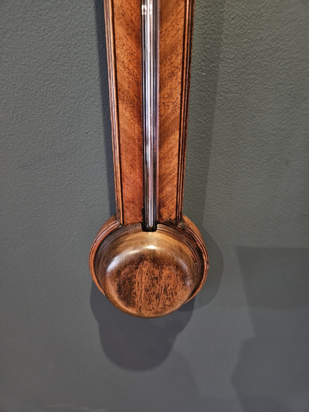 A wall-mounted Georgian mahogany stick barometer featuring a broken-arch pediment, a silvered register plate behind glass, and a turned cistern cover at the base. View V