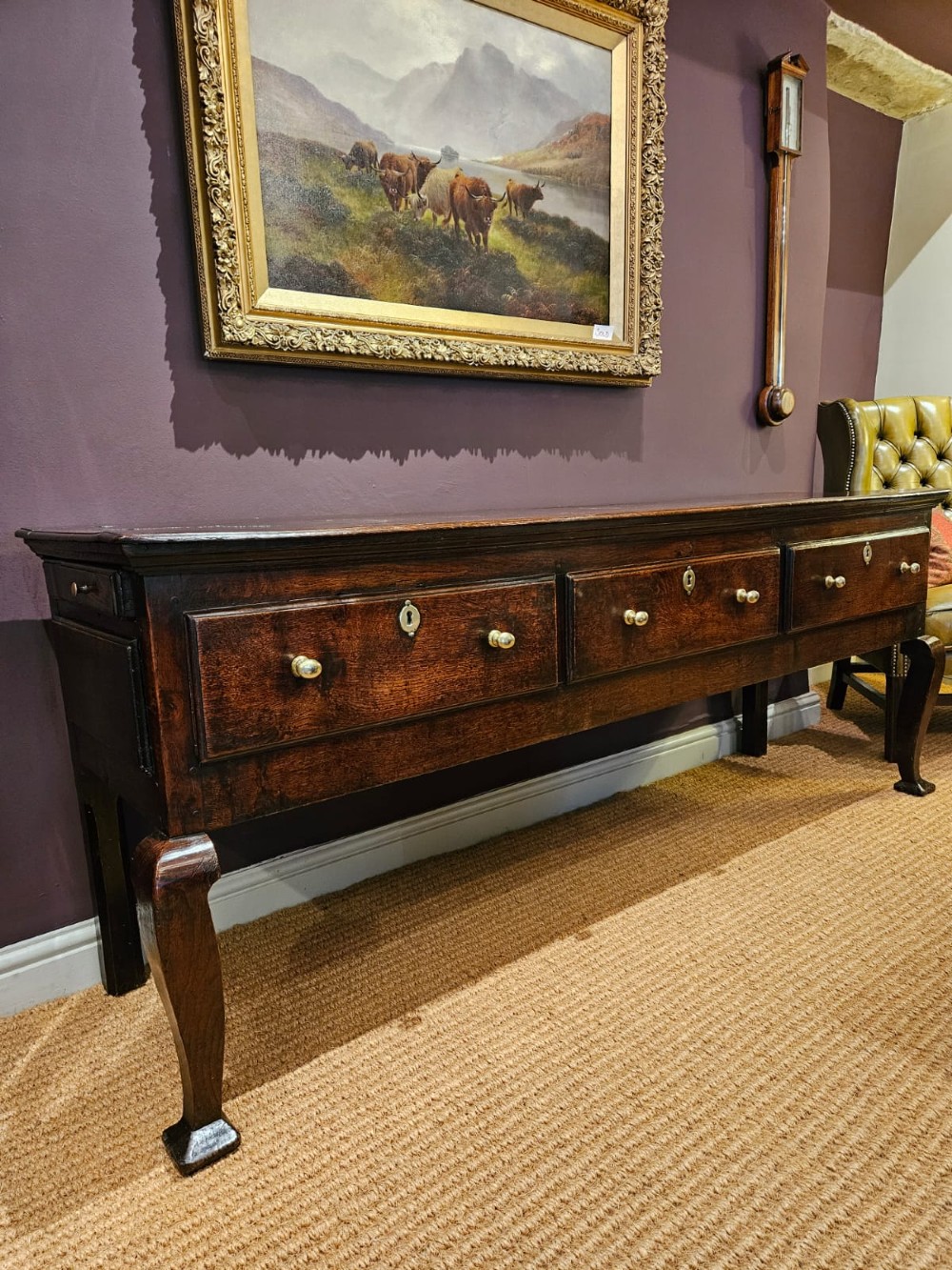 A low George II dark oak dresser base featuring three inline drawers with brass knob handles, set on front cabriole legs.