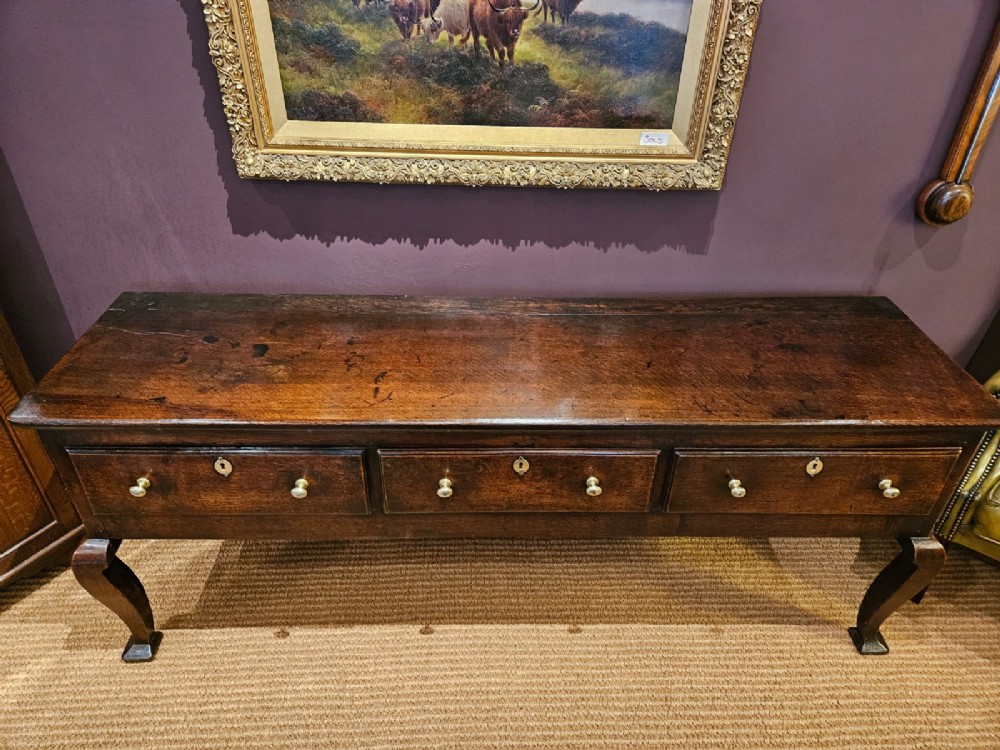 A low George II dark oak dresser base featuring three inline drawers with brass knob handles, set on front cabriole legs. View II