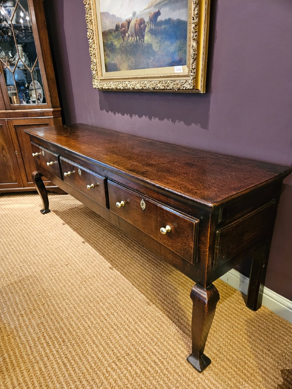 A low George II dark oak dresser base featuring three inline drawers with brass knob handles, set on front cabriole legs. View IV