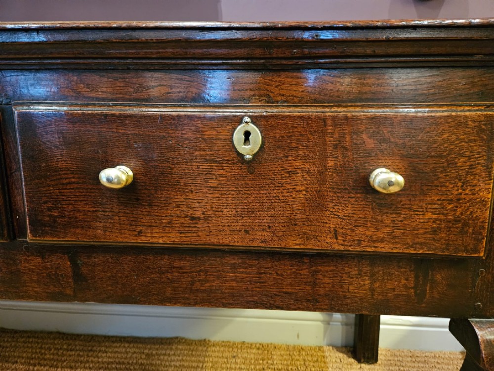 A low George II dark oak dresser base featuring three inline drawers with brass knob handles, set on front cabriole legs. View V