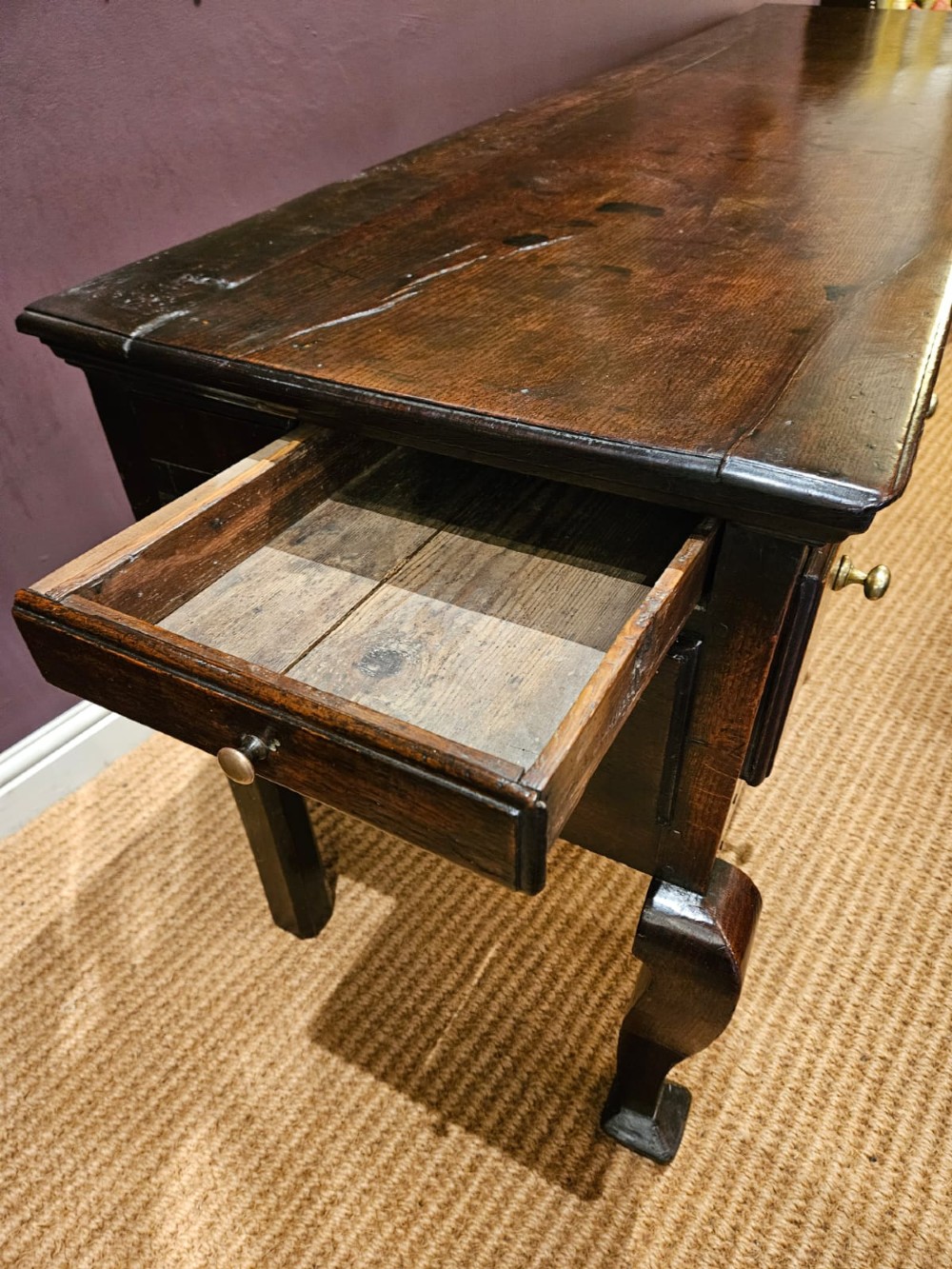 A low George II dark oak dresser base featuring three inline drawers with brass knob handles, set on front cabriole legs. View VII