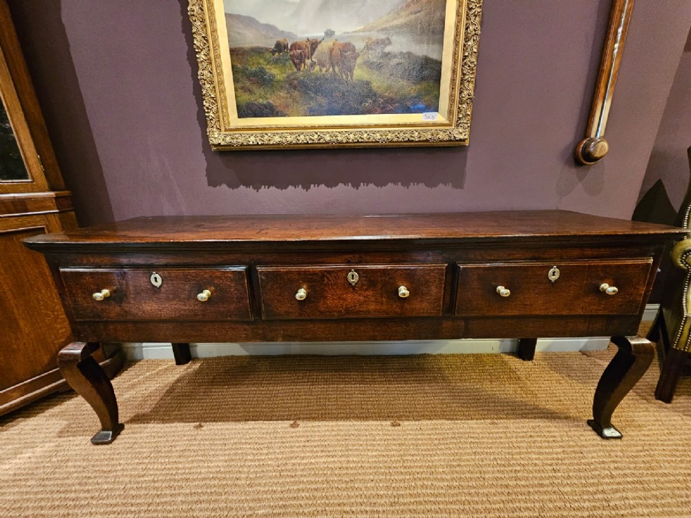 A low George II dark oak dresser base featuring three inline drawers with brass knob handles, set on front cabriole legs. View VIII
