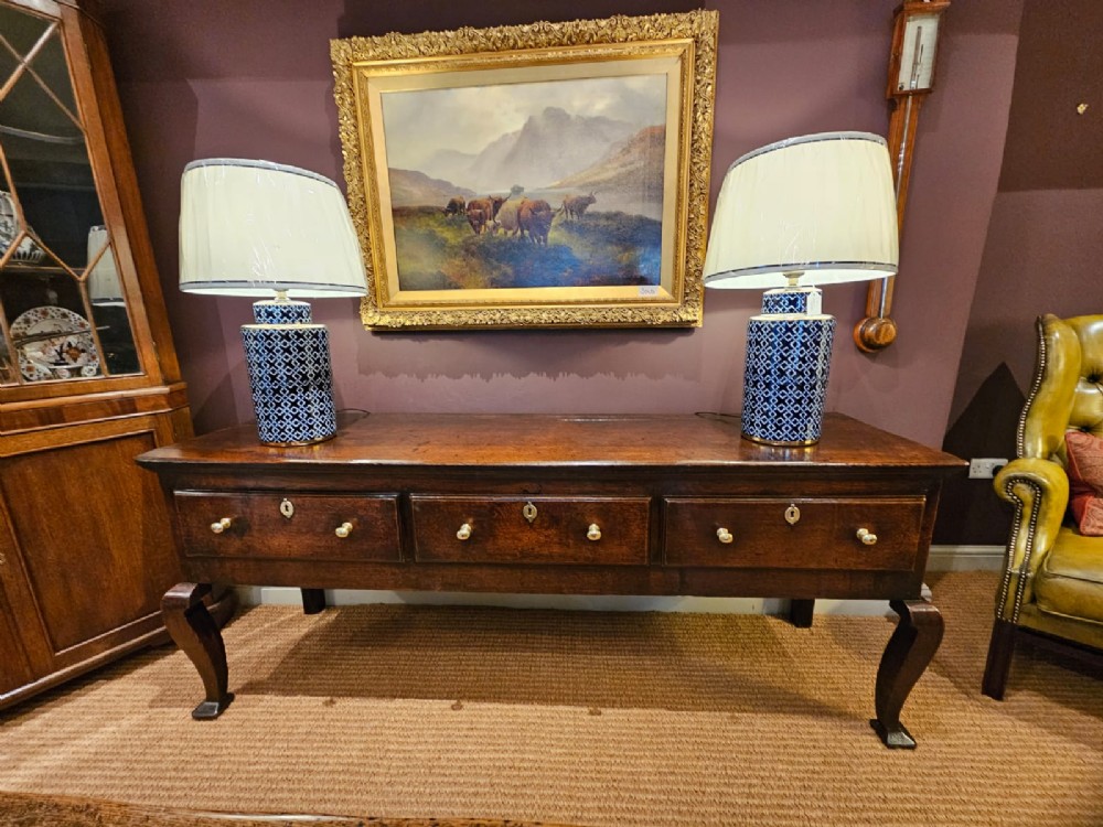 A low George II dark oak dresser base featuring three inline drawers with brass knob handles, set on front cabriole legs. View X
