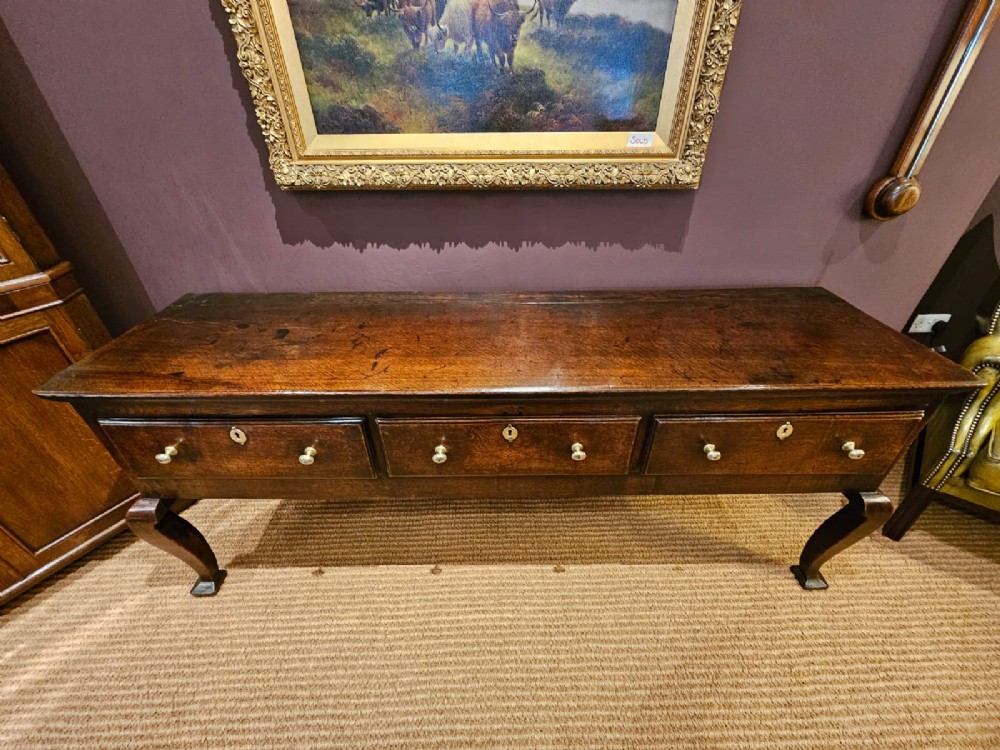 A low George II dark oak dresser base featuring three inline drawers with brass knob handles, set on front cabriole legs. View XI