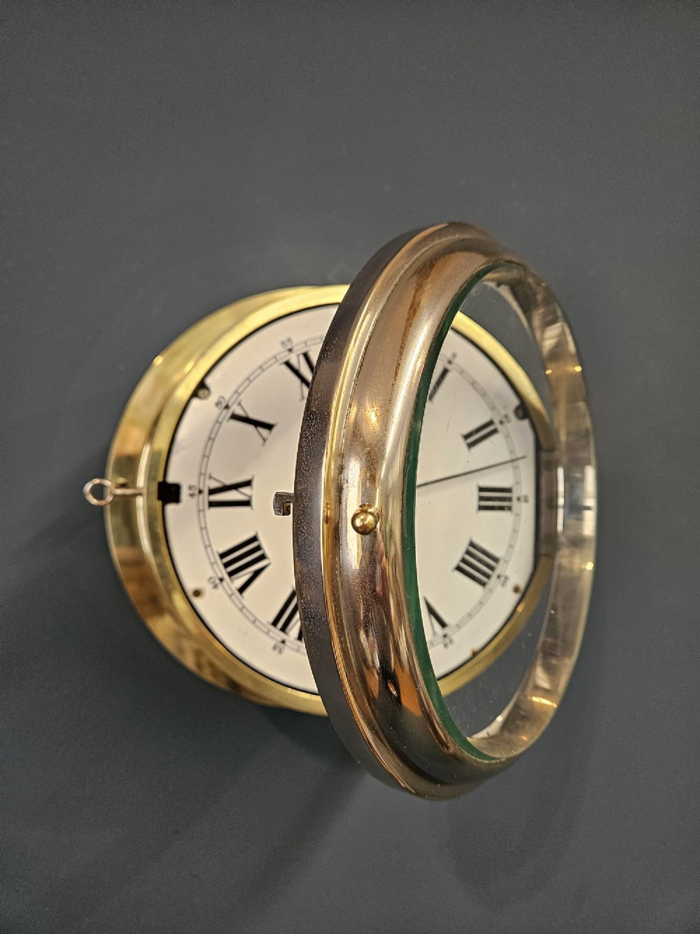 An antique circular brass ships clock with a white enamel dial, black Roman numerals, and a central seconds sweep hand. View II