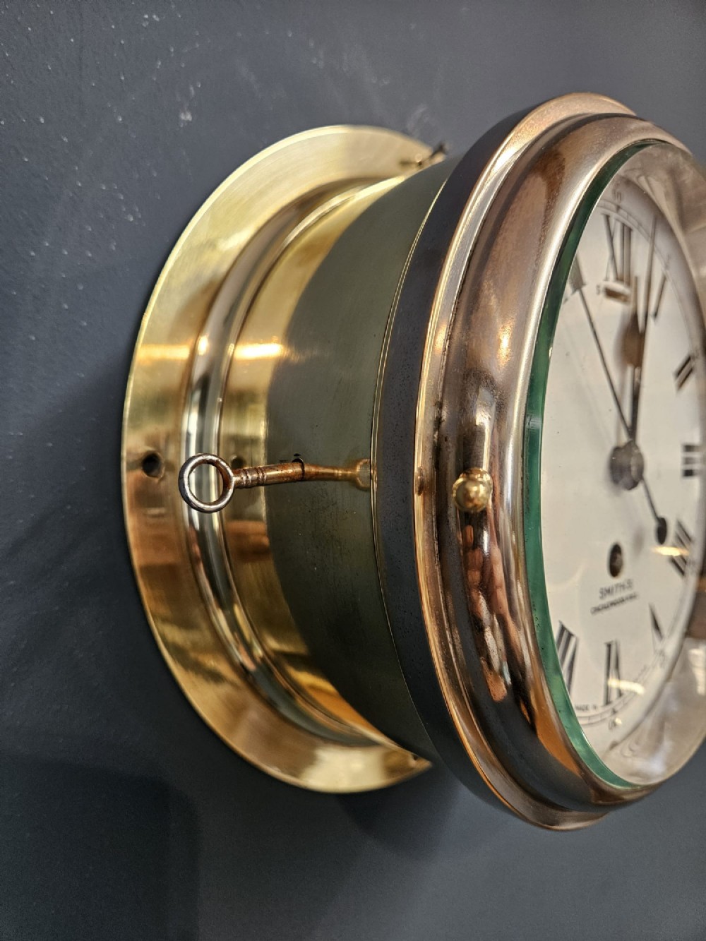 An antique circular brass ships clock with a white enamel dial, black Roman numerals, and a central seconds sweep hand. View III