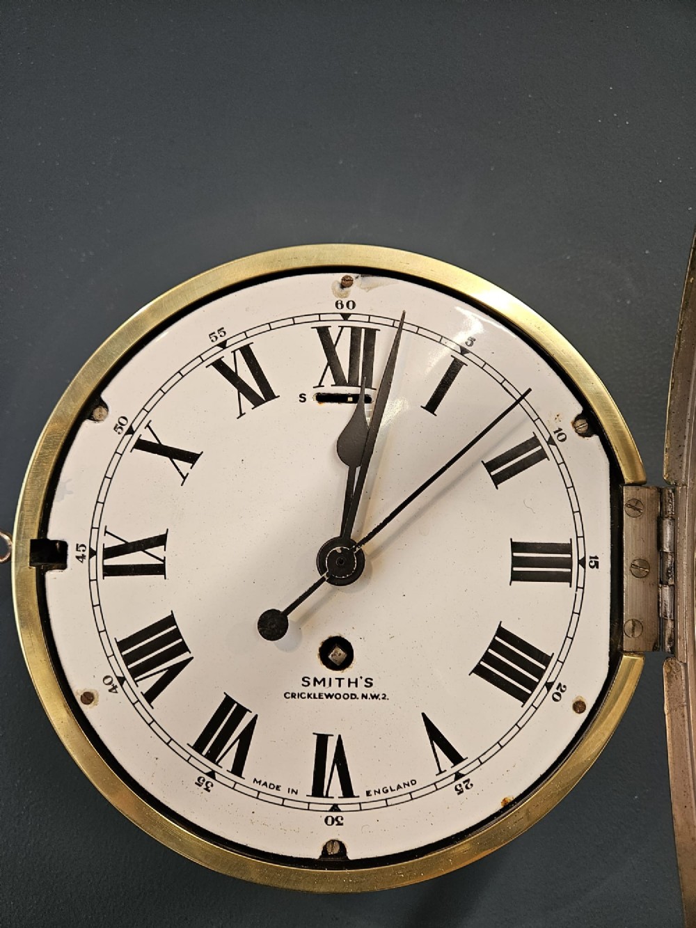 An antique circular brass ships clock with a white enamel dial, black Roman numerals, and a central seconds sweep hand. View IV