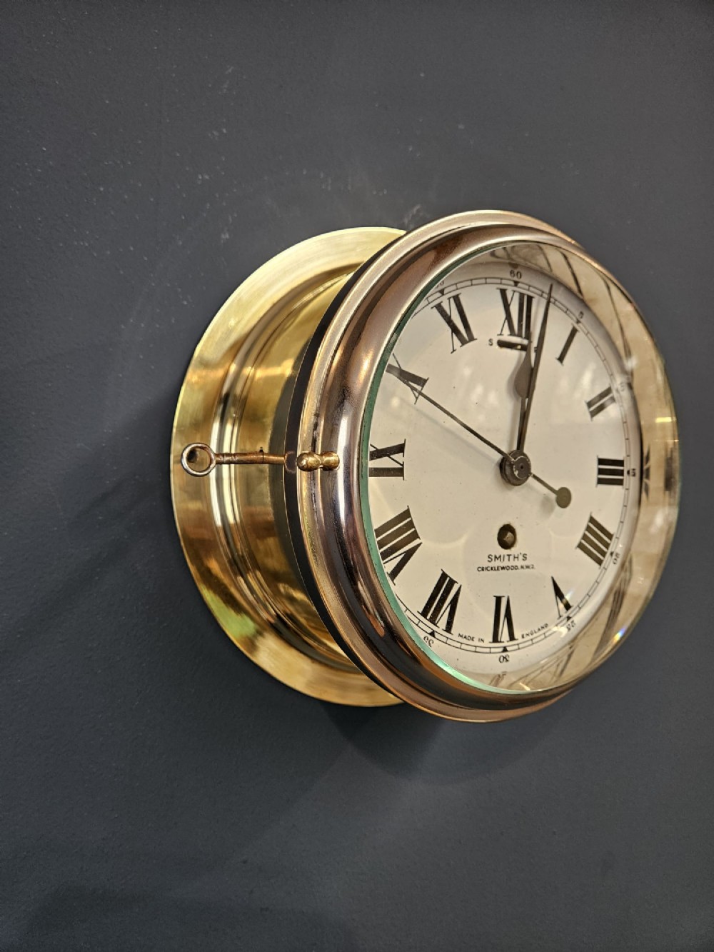 An antique circular brass ships clock with a white enamel dial, black Roman numerals, and a central seconds sweep hand. View VI