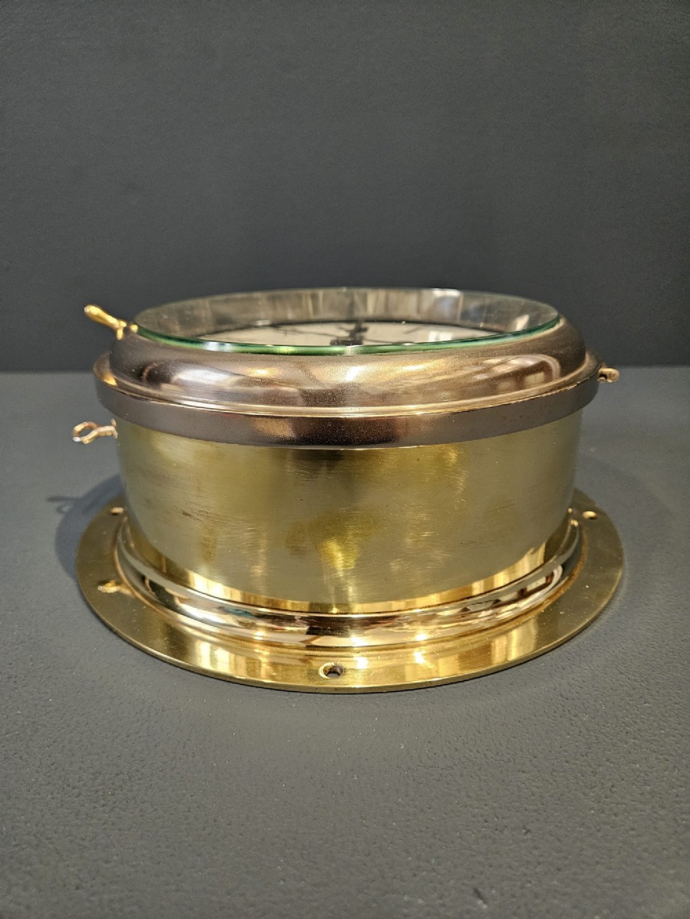 An antique circular brass ships clock with a white enamel dial, black Roman numerals, and a central seconds sweep hand. View VII