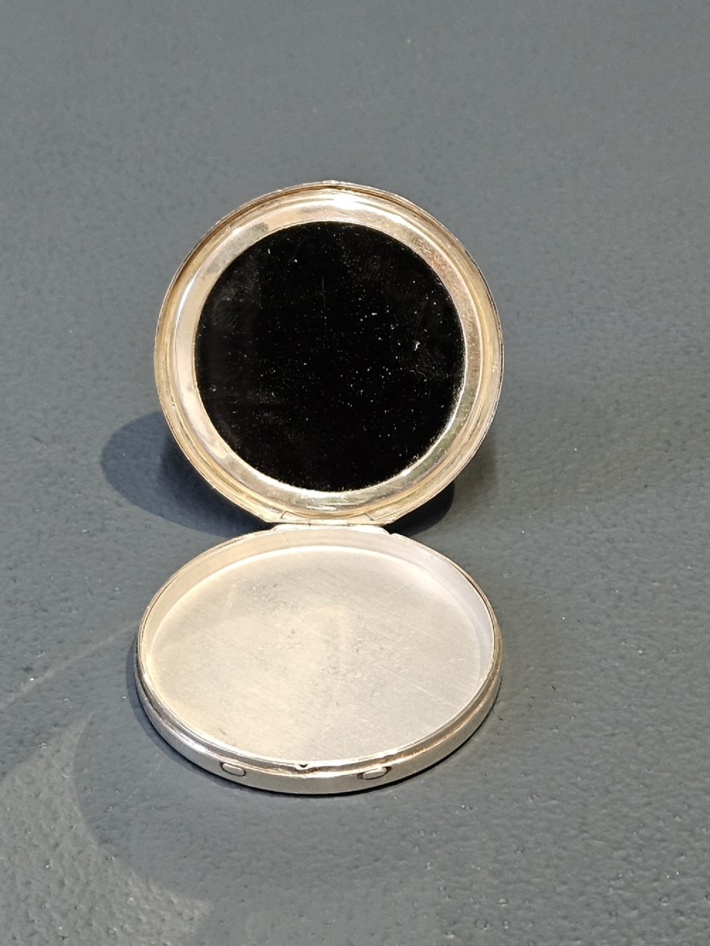 A circular silver compact featuring a vibrant blue engine-turned guilloche enamel lid with a radiating pattern. View III