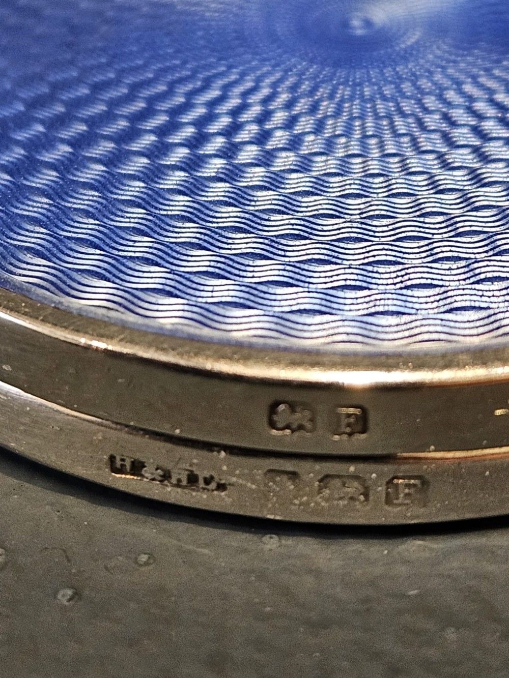 A circular silver compact featuring a vibrant blue engine-turned guilloche enamel lid with a radiating pattern. View VI
