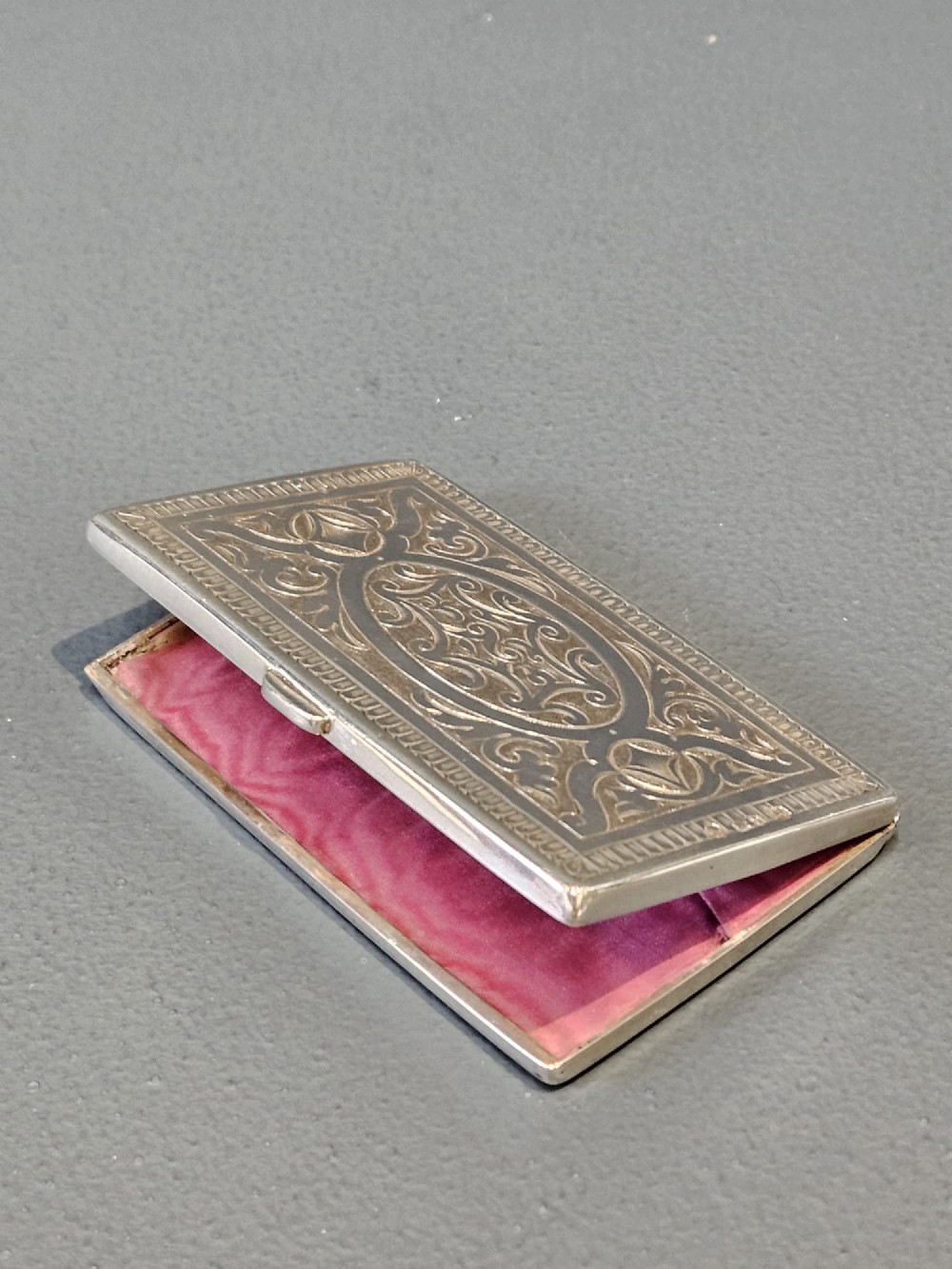 A rectangular Victorian silver card case featuring hand-engraved scrolling foliage, an oval central medallion, and a hinged side edge. View III