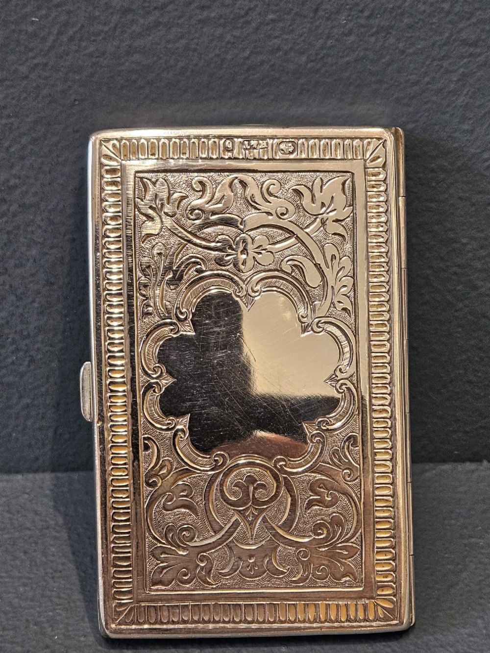 A rectangular Victorian silver card case featuring hand-engraved scrolling foliage, an oval central medallion, and a hinged side edge. View VI
