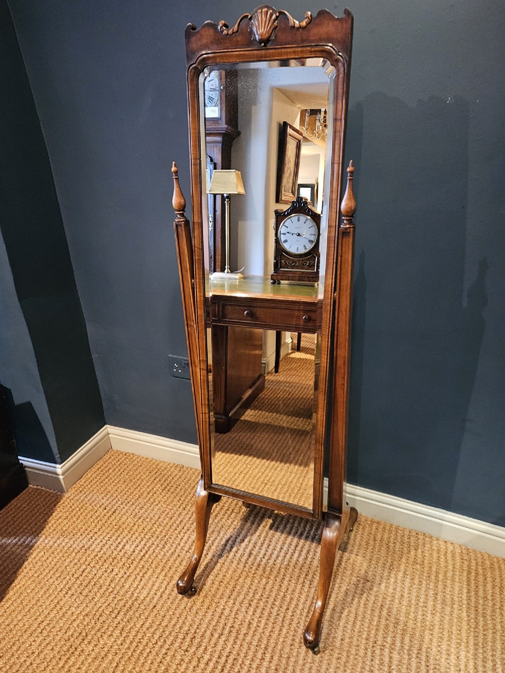 A George III style mahogany cheval mirror featuring an arched top with a carved shell cresting, turned side finials, and splayed legs on brass castors.