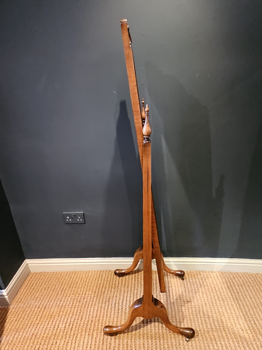 A George III style mahogany cheval mirror featuring an arched top with a carved shell cresting, turned side finials, and splayed legs on brass castors. View II