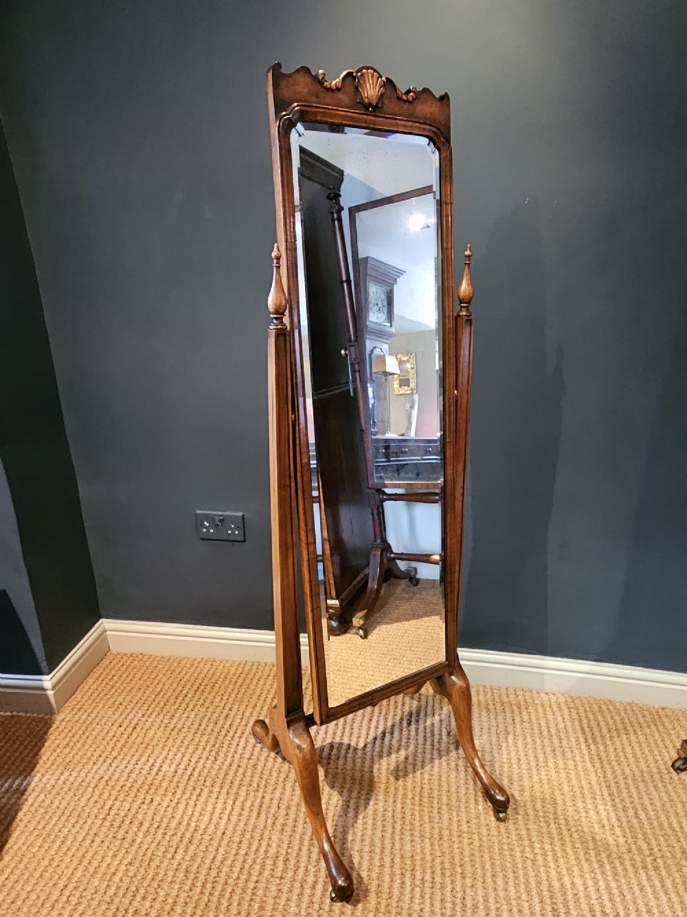 A George III style mahogany cheval mirror featuring an arched top with a carved shell cresting, turned side finials, and splayed legs on brass castors. View IV