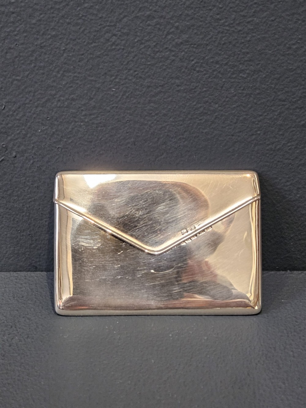 An antique sterling silver envelope-shaped card case with visible hallmarks along the flap seam resting against a dark grey backdrop.