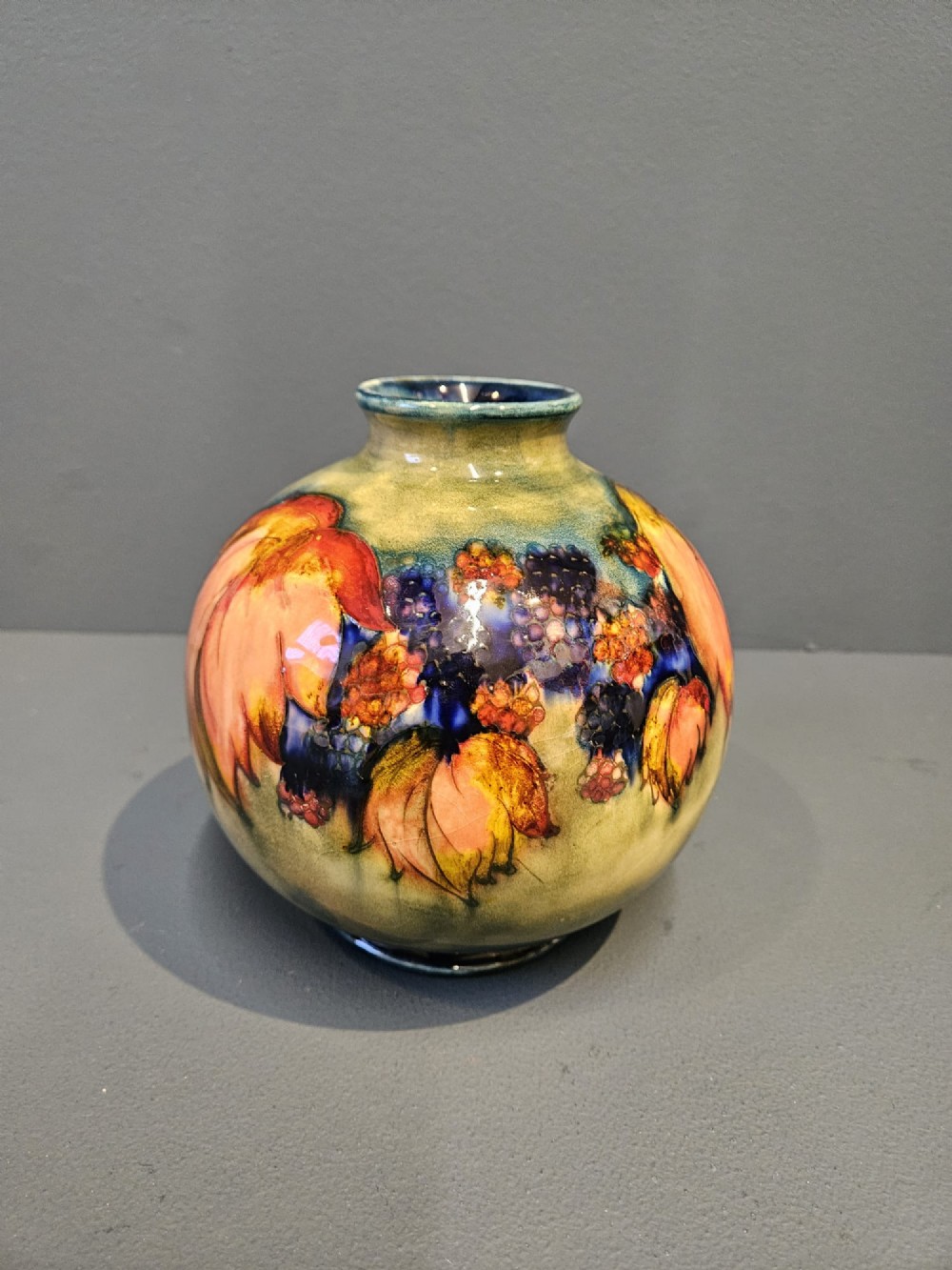 A spherical Moorcroft pottery vase decorated with a tubelined leaf and blackberry pattern under a glossy flambe glaze.