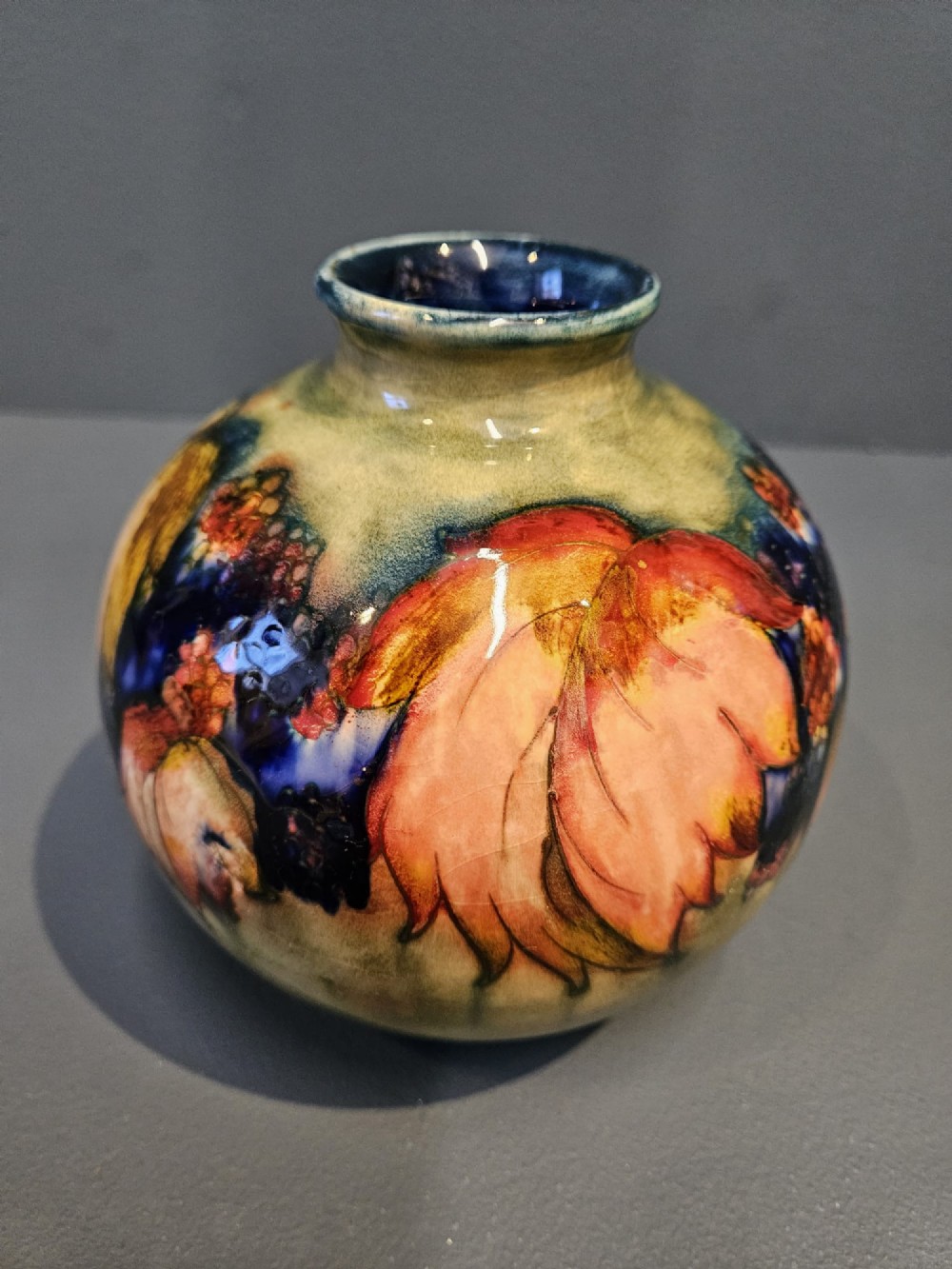 A spherical Moorcroft pottery vase decorated with a tubelined leaf and blackberry pattern under a glossy flambe glaze. View II