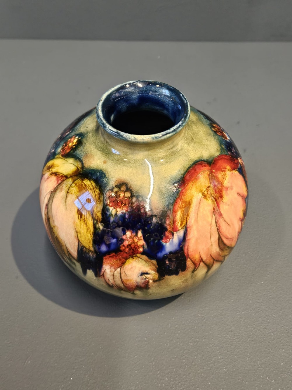 A spherical Moorcroft pottery vase decorated with a tubelined leaf and blackberry pattern under a glossy flambe glaze. View V