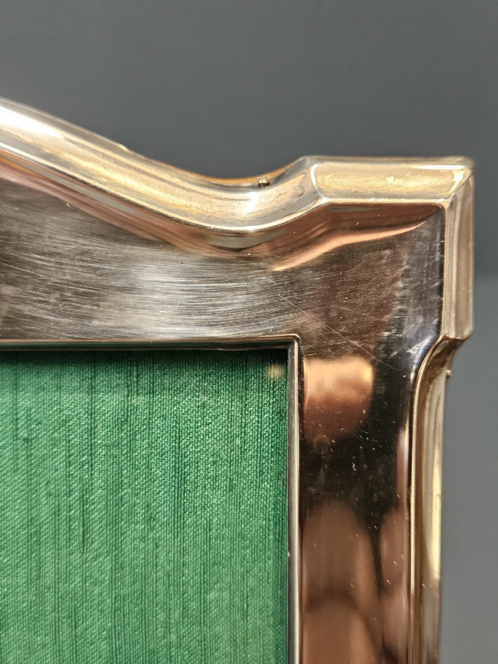 A sterling silver photo frame featuring a swept arched top, moulded border, visible hallmarks at the base, and a green fabric backing. View V