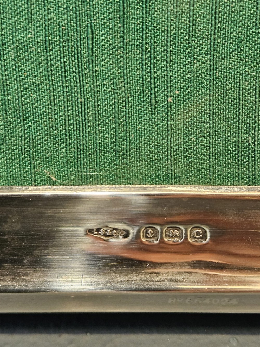 A sterling silver photo frame featuring a swept arched top, moulded border, visible hallmarks at the base, and a green fabric backing. View VI