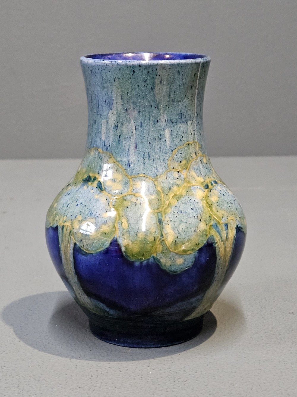 A small baluster-shaped ceramic vase featuring tubelined tree motifs in tones of green and turquoise over a deep cobalt blue glaze.