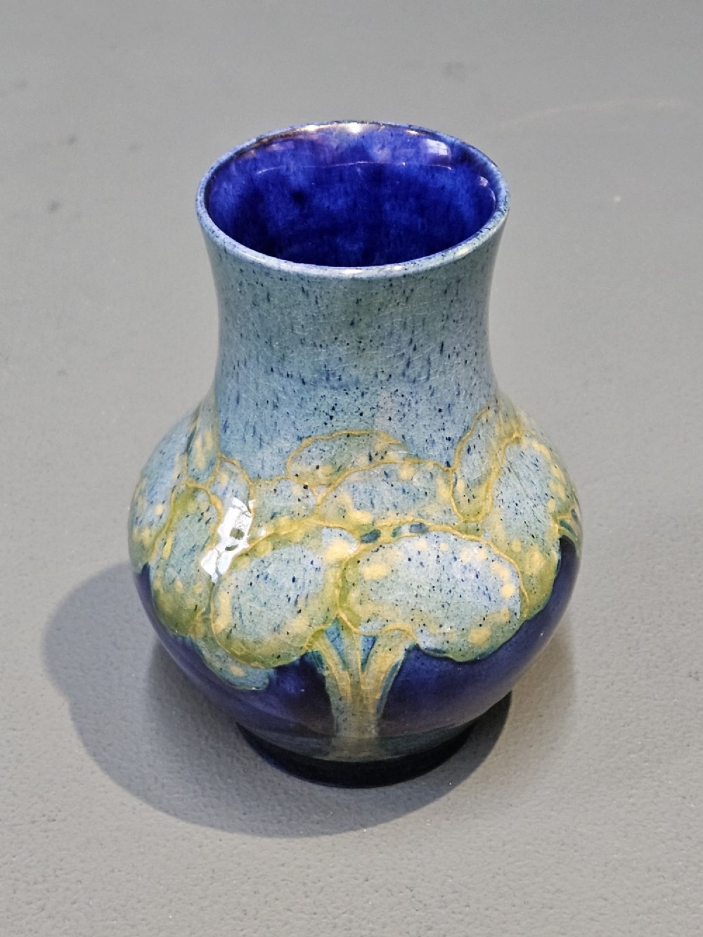 A small baluster-shaped ceramic vase featuring tubelined tree motifs in tones of green and turquoise over a deep cobalt blue glaze. View III