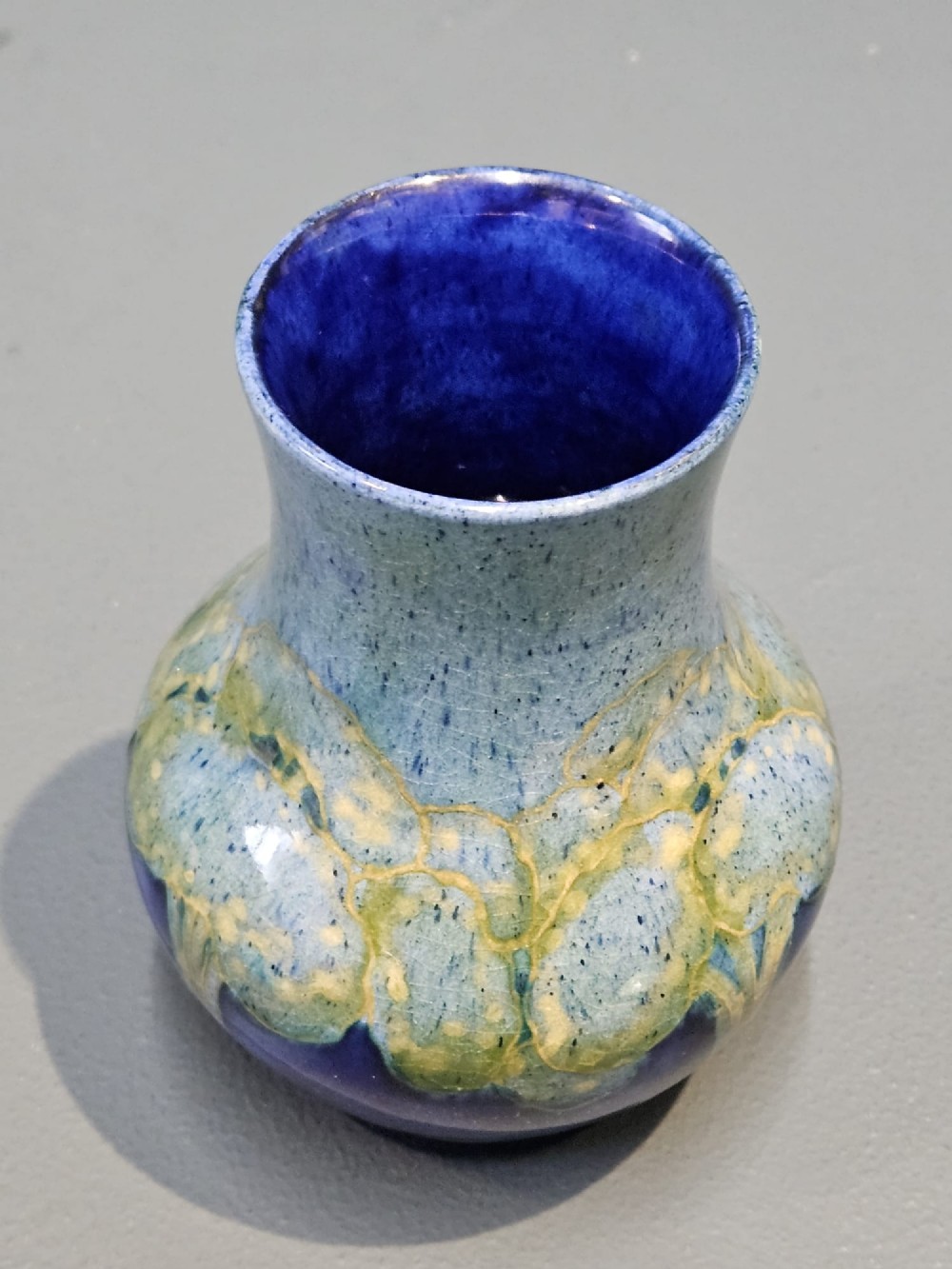 A small baluster-shaped ceramic vase featuring tubelined tree motifs in tones of green and turquoise over a deep cobalt blue glaze. View V
