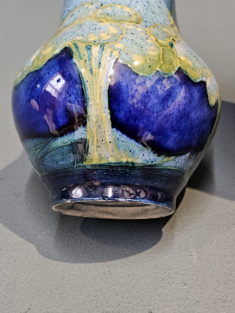 A small baluster-shaped ceramic vase featuring tubelined tree motifs in tones of green and turquoise over a deep cobalt blue glaze. View VI