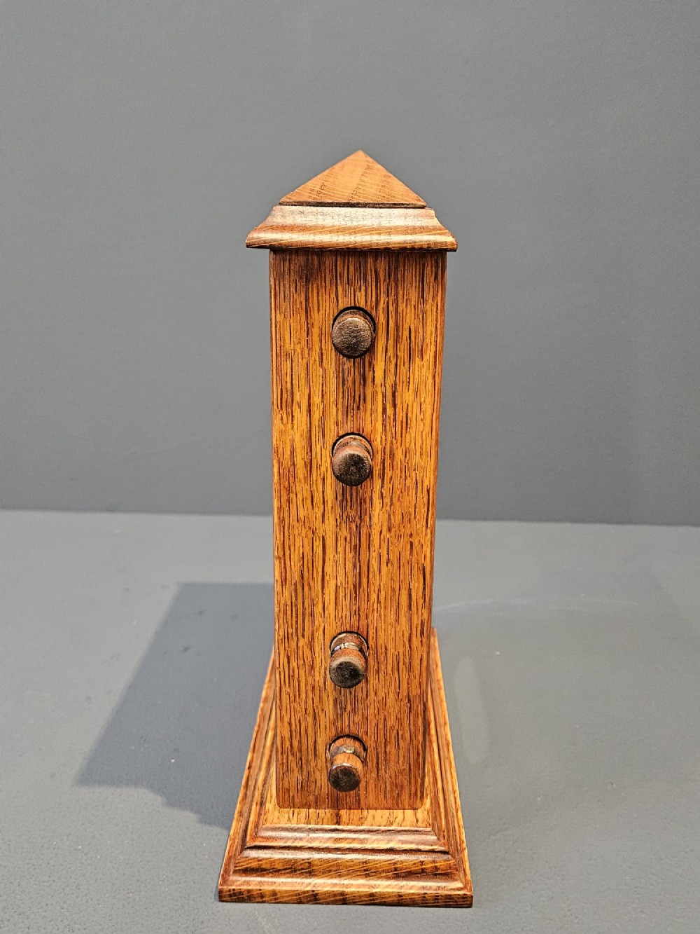 An Edwardian figured oak perpetual desk calendar featuring a pediment top, moulded base, three display apertures, and turned wooden side knobs. View II