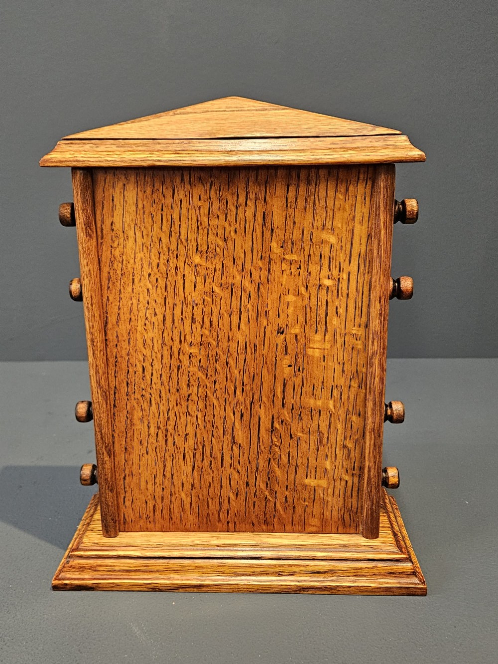 An Edwardian figured oak perpetual desk calendar featuring a pediment top, moulded base, three display apertures, and turned wooden side knobs. View VII