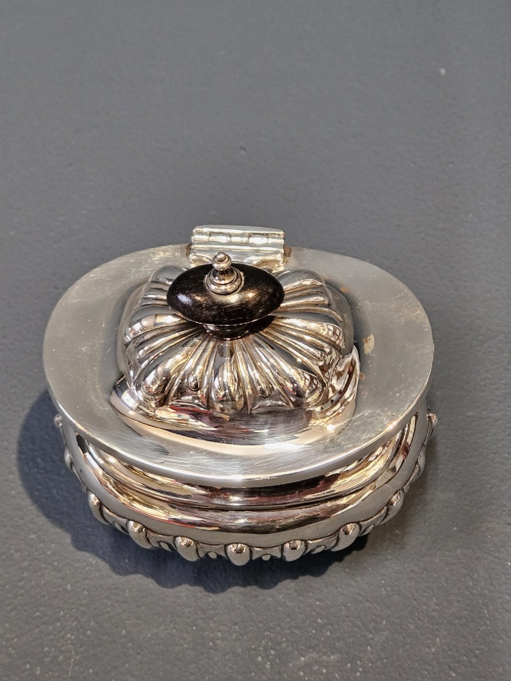 A George V polished sterling silver tea caddy featuring a fluted lower body, hinged lid, ebonised finial, and stamped hallmarks. View V