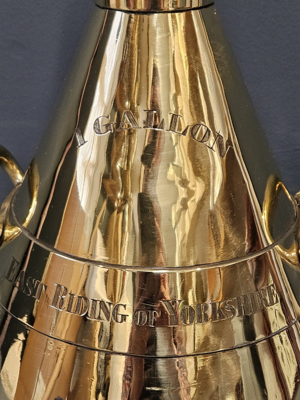 A polished Victorian brass one gallon capacity standard measure with a flared funnel top, conical body, twin loop handles, and official engravings. View IV