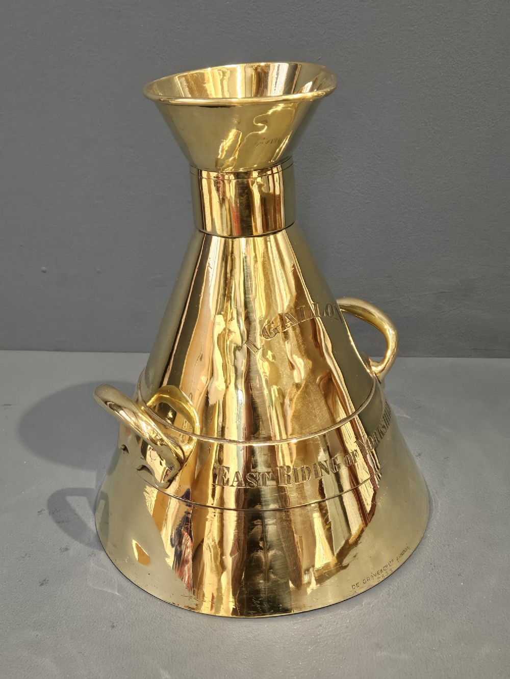 A polished Victorian brass one gallon capacity standard measure with a flared funnel top, conical body, twin loop handles, and official engravings. View IX