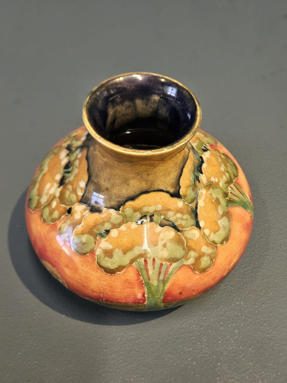 A small squat earthenware Moorcroft Eventide vase featuring tubelined trees against an orange and ochre twilight ground. View II