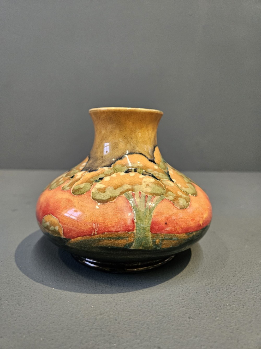 A small squat earthenware Moorcroft Eventide vase featuring tubelined trees against an orange and ochre twilight ground. View III