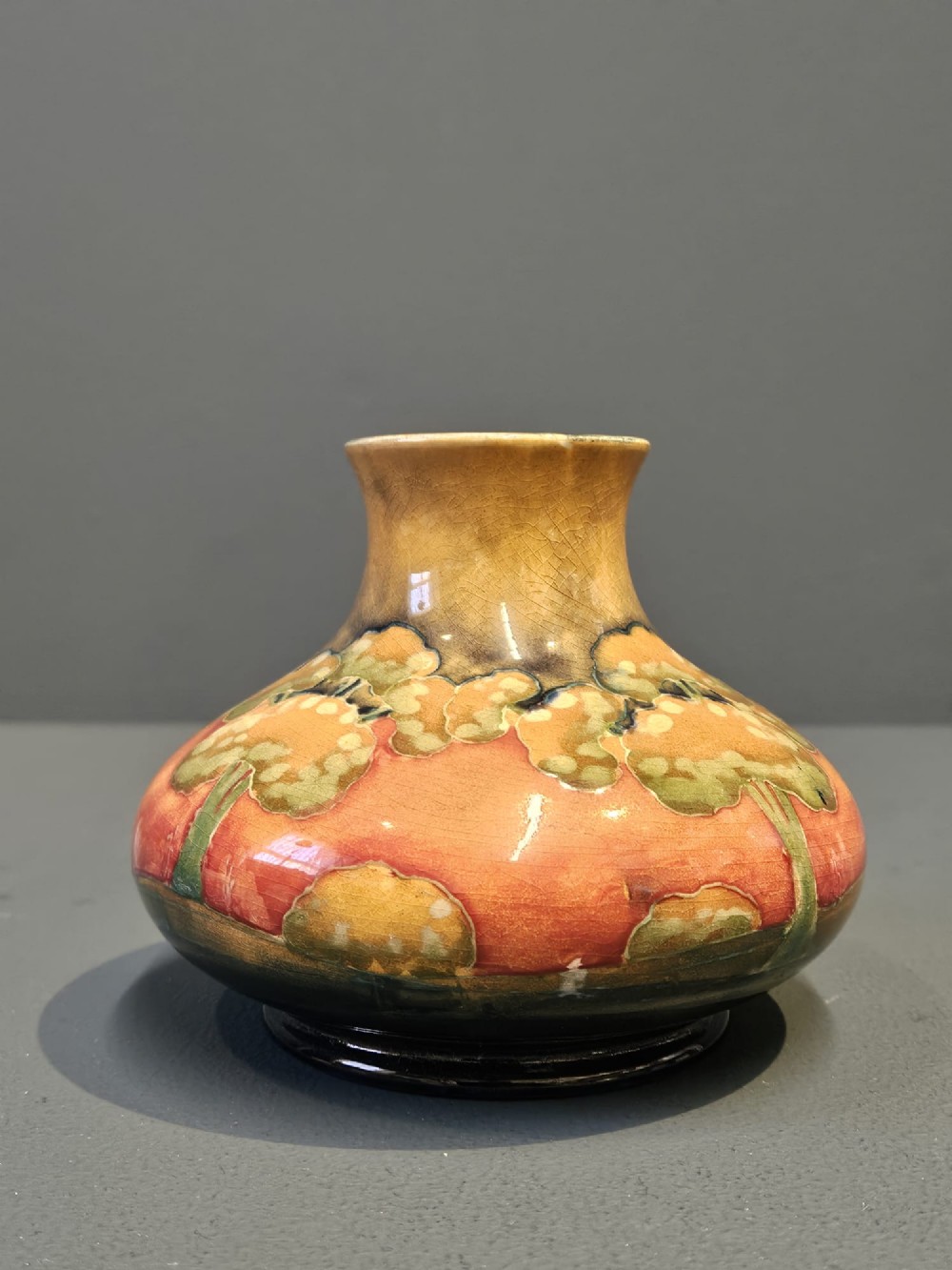 A small squat earthenware Moorcroft Eventide vase featuring tubelined trees against an orange and ochre twilight ground. View VI