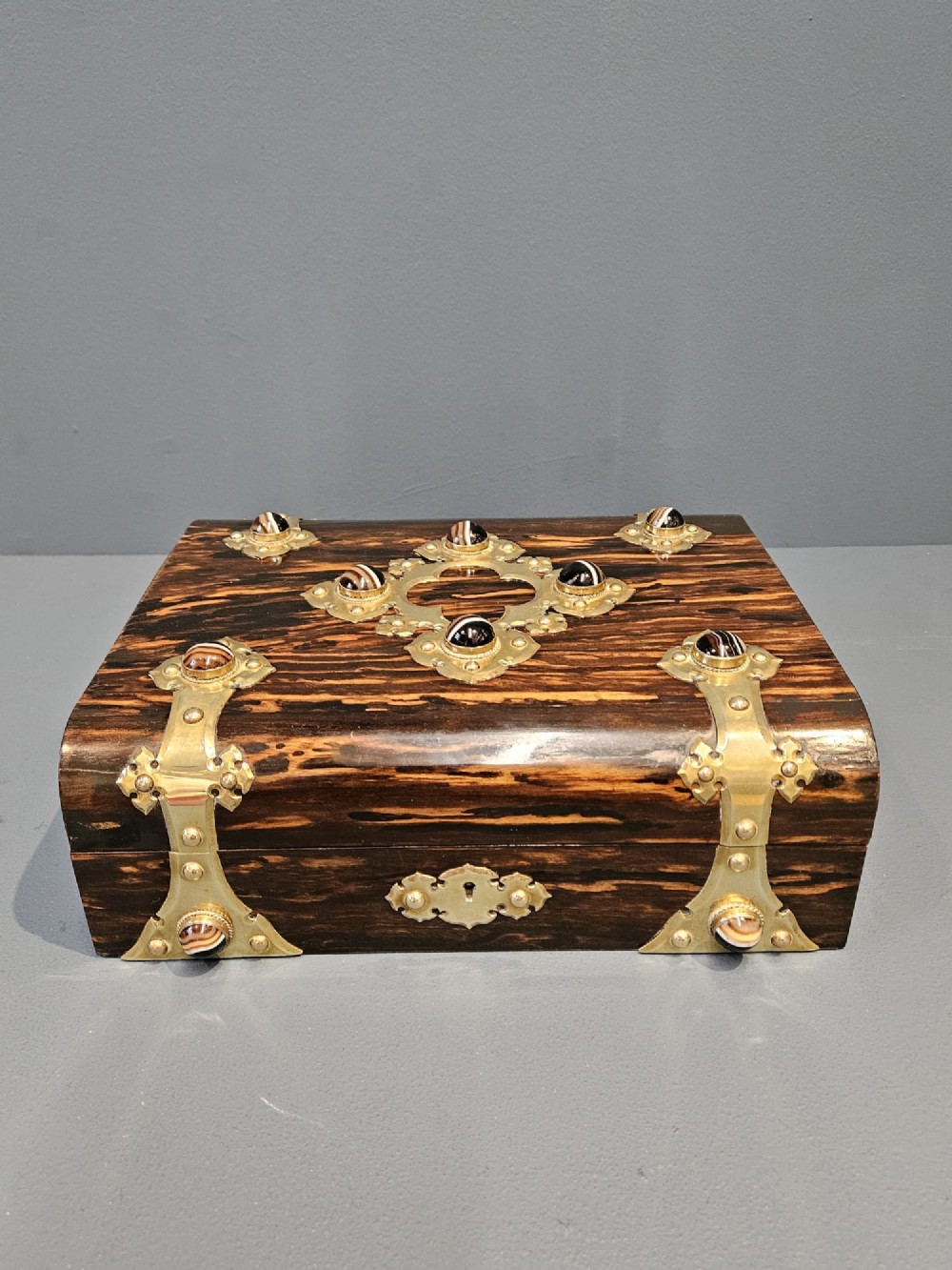 A dark coromandel wood box featuring decorative brass strapwork inset with rounded agate cabochons. View II