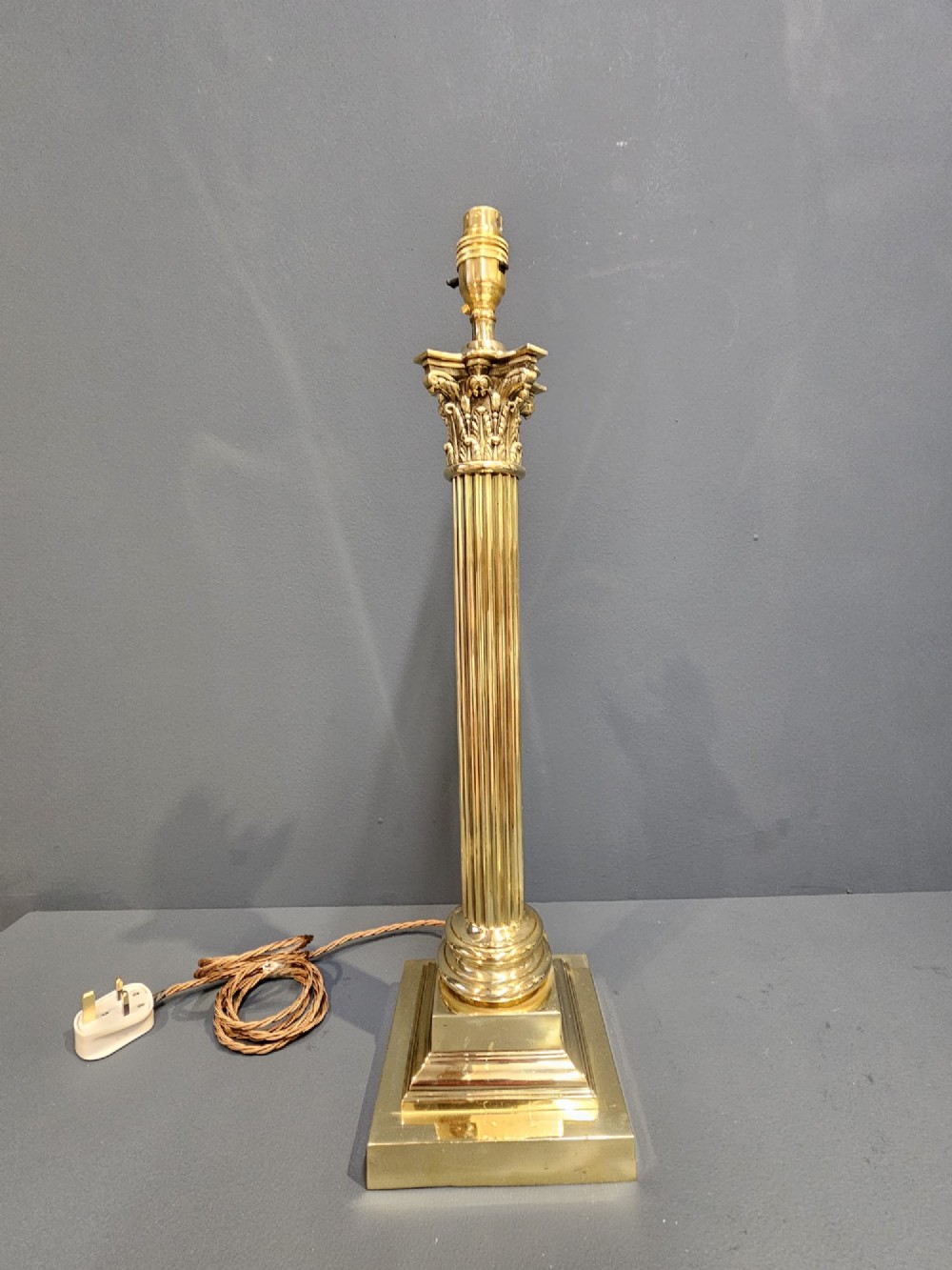 An Edwardian brass table lamp designed as a classical Corinthian column with a fluted shaft and stepped square base.