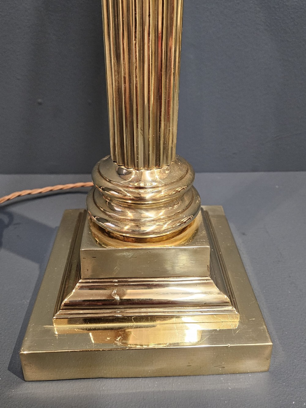 An Edwardian brass table lamp designed as a classical Corinthian column with a fluted shaft and stepped square base. View II