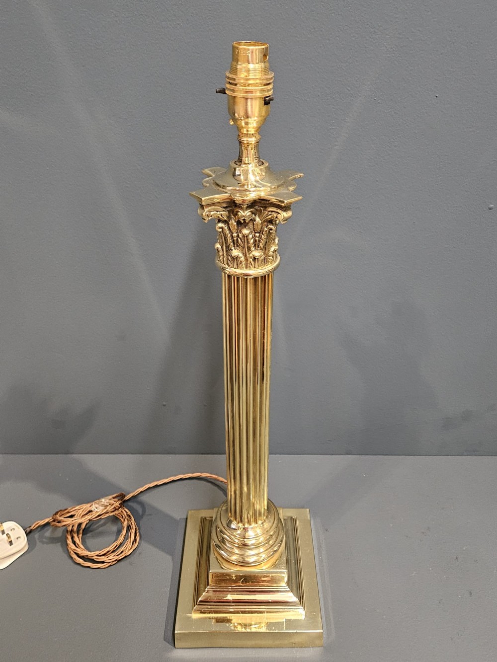 An Edwardian brass table lamp designed as a classical Corinthian column with a fluted shaft and stepped square base. View III